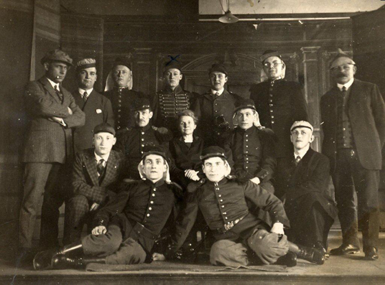 Ein altes Schwarz-Weiß-Foto mit sechzehn Männern und einer Frau, einige in Wehruniform, andere im Anzug. Die Szene in einem prunkvollen Innenraum bietet einen seltenen Einblick in die Geschichte der Wehr aus einer vergangenen Epoche.